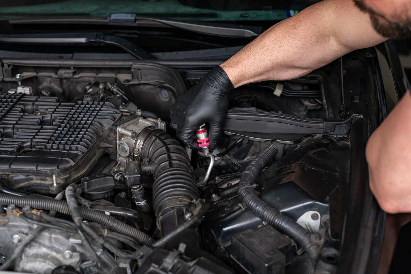 Gloved hand applying AC refrigerant leak sealer to car engine service valve