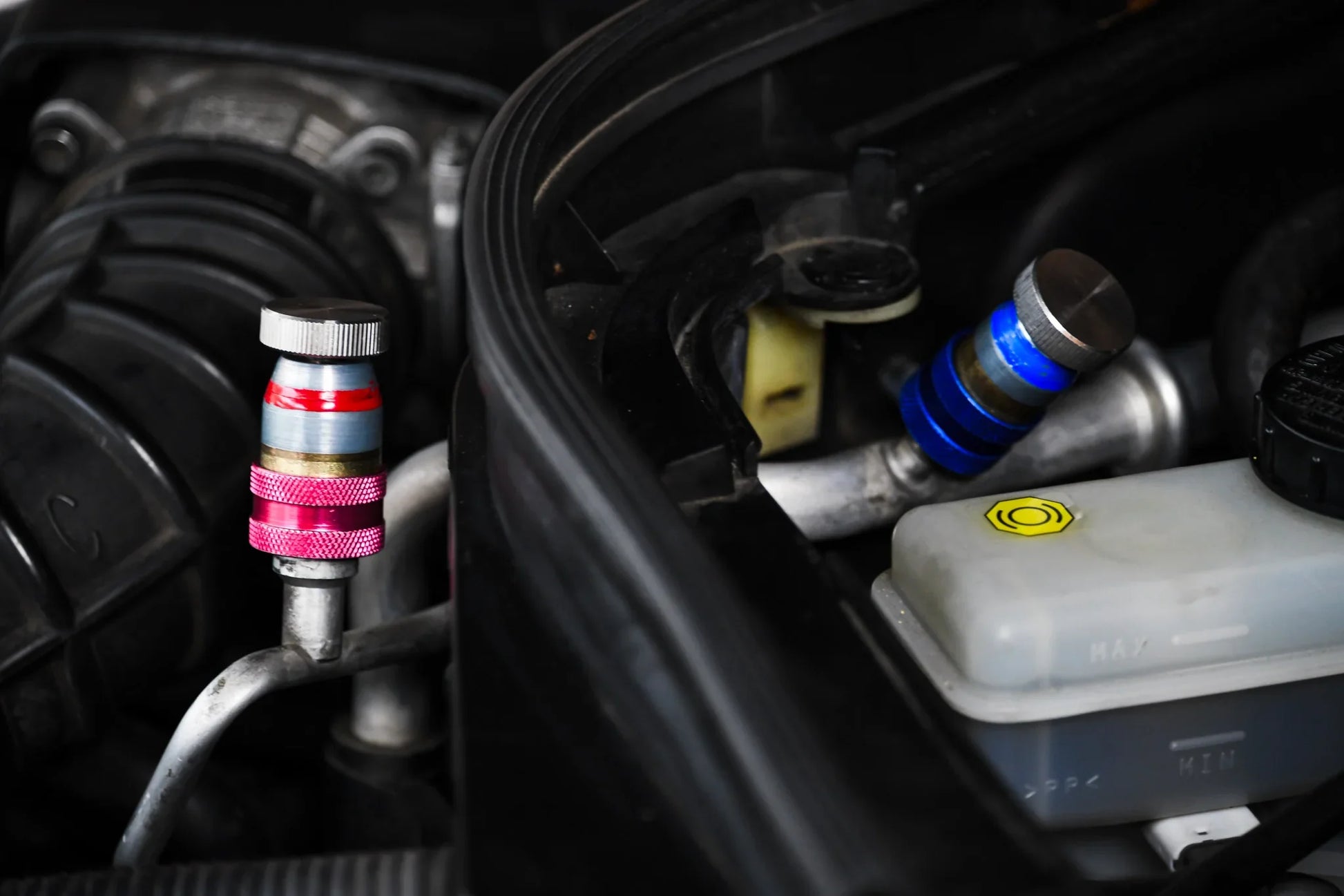 Close-up of car AC service valve caps, red and blue, on a vehicle engine bay