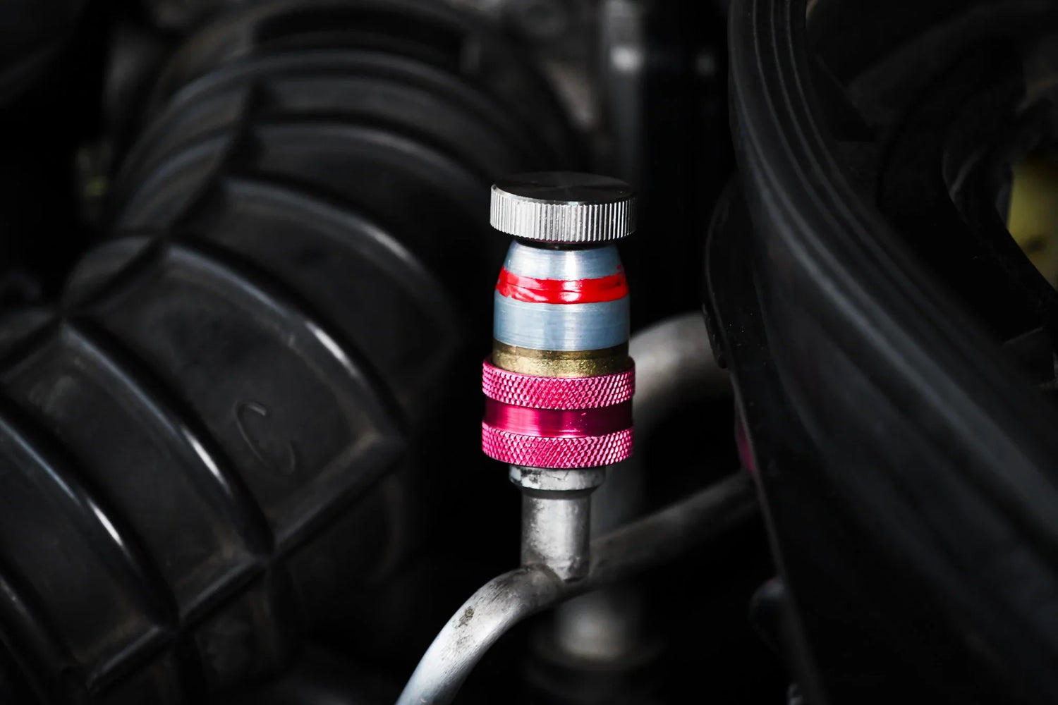 Close-up of car AC service valve with red and blue cap for refrigerant leak repair