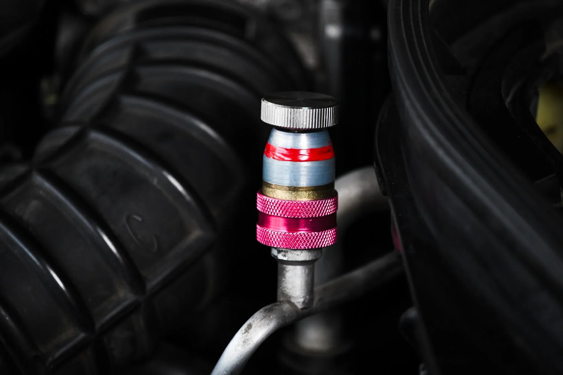 Close-up of car AC service valve with red and blue cap for refrigerant leak repair