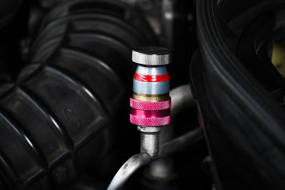 Close-up of car AC service valve with red and blue cap for refrigerant leak repair