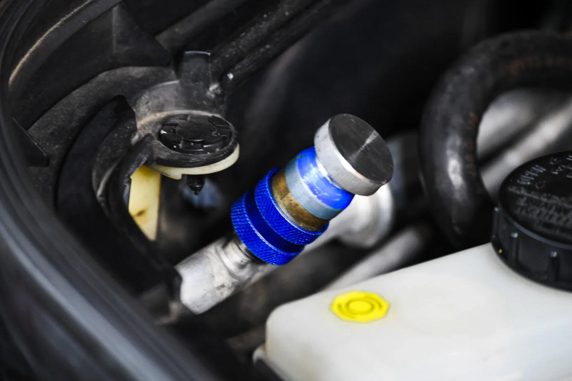 Close-up of car AC service valve with blue cap for refrigerant leak repair
