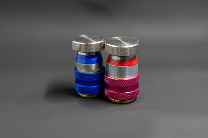 Two metal car AC refrigerant service valve caps, one blue and one red, on a gray background