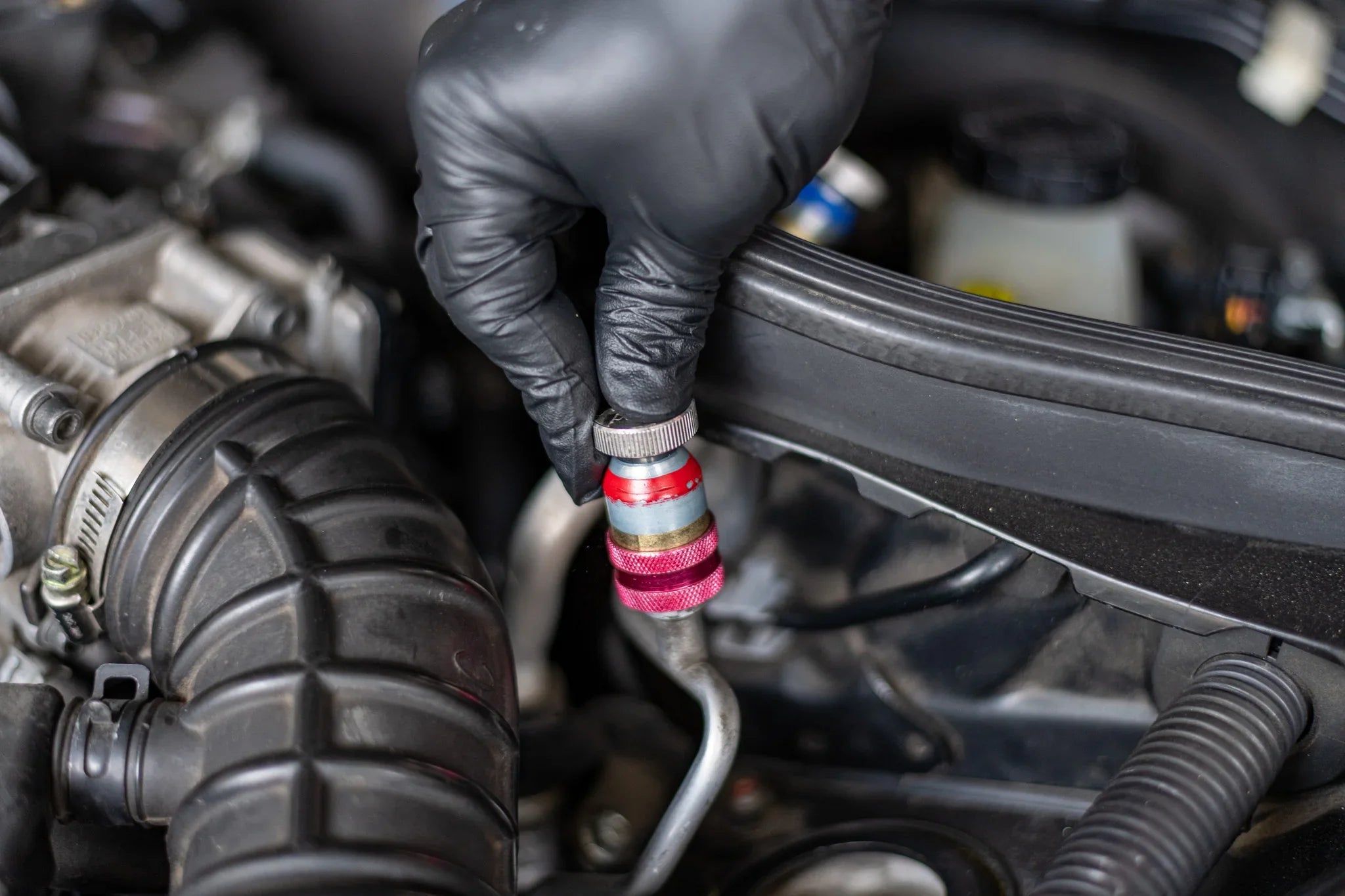 Hand with black glove attaching AC refrigerant valve tool to car air conditioning line