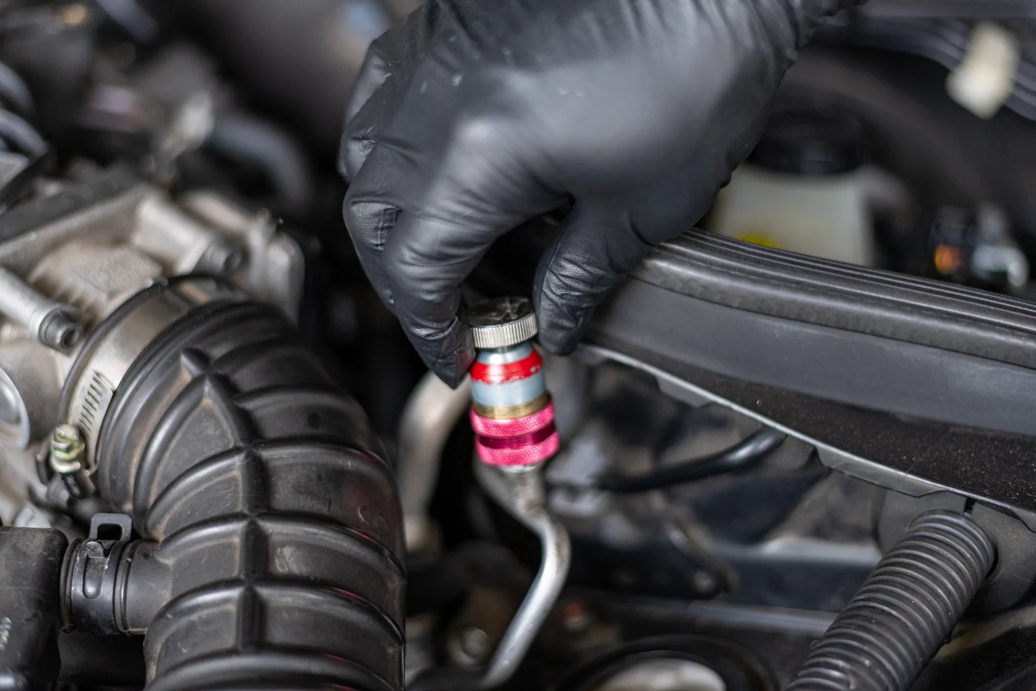 Gloved hand repairing car AC refrigerant service valve under the hood