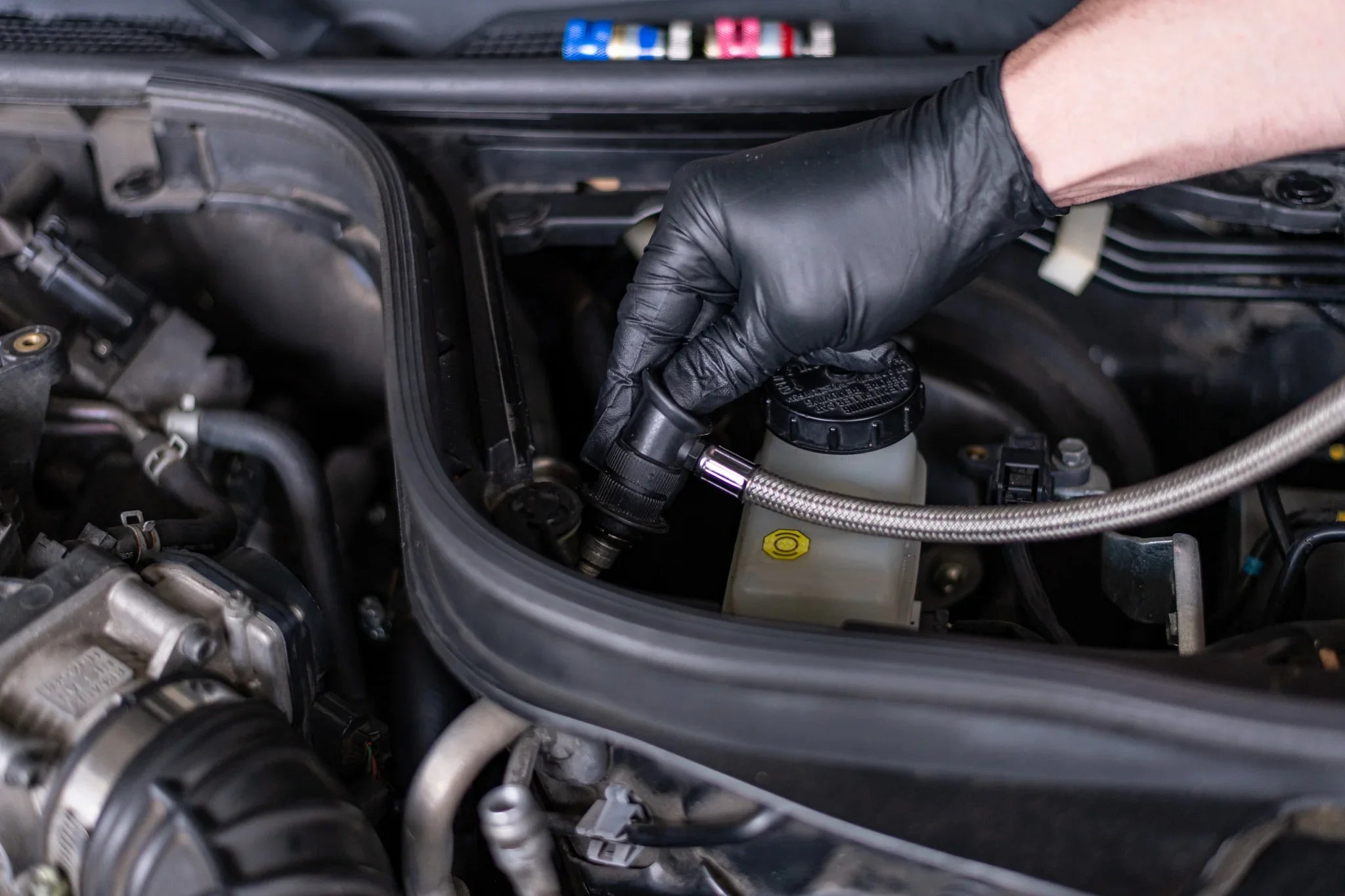 Gloved hand applying AC refrigerant leak repair tool to car service valve under hood