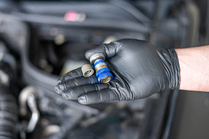 Gloved hand holding a car AC service valve and cap for refrigerant leak repair