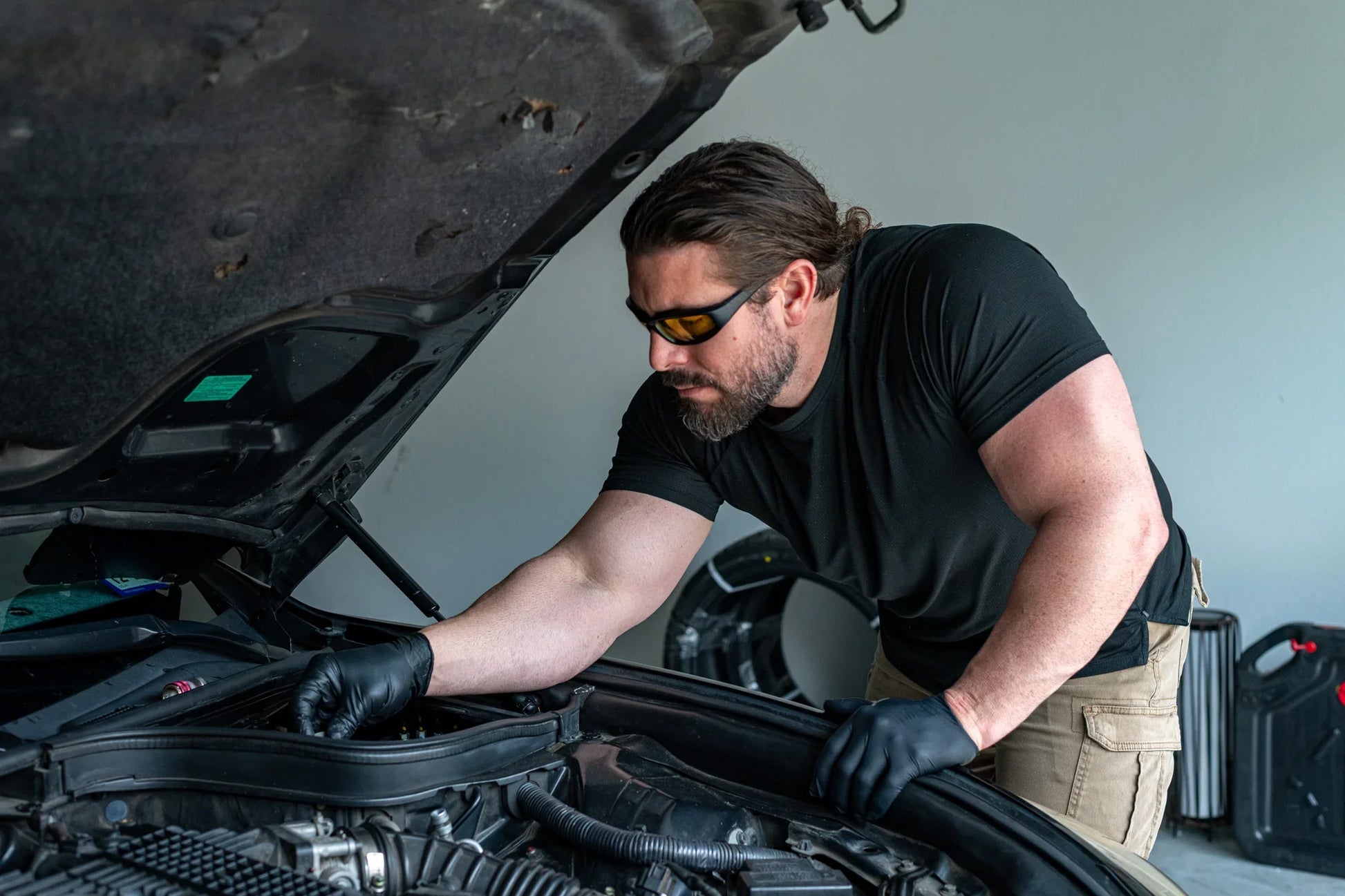 Man in black gloves repairing car AC under hood, vehicle maintenance in garage